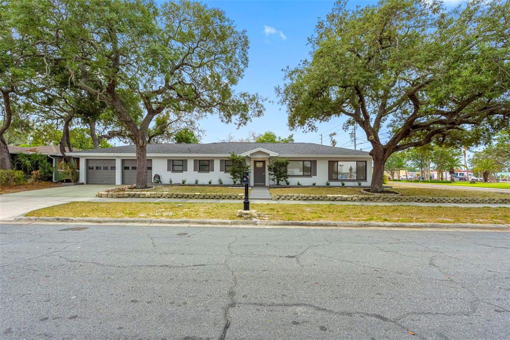 A single-story house with a gray exterior, two-car garage, and large oak trees in front — 1005 APACHE TRAIL, CLEARWATER, FL