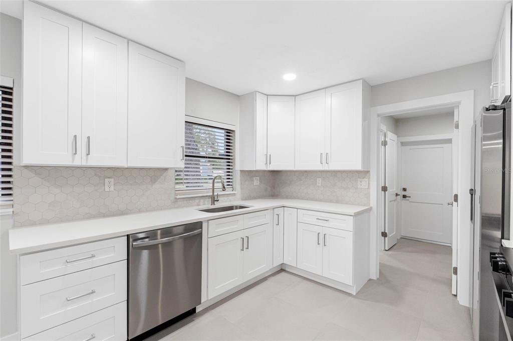 A modern kitchen features white cabinets, stainless steel appliances, and a light-colored hexagonal tile backsplash — 1005 APACHE TRAIL, CLEARWATER, FL