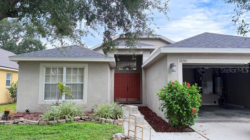 A single-story house features a red double front door, a garage, and a landscaped yard — 1120 VINETREE DRIVE, BRANDON, FL