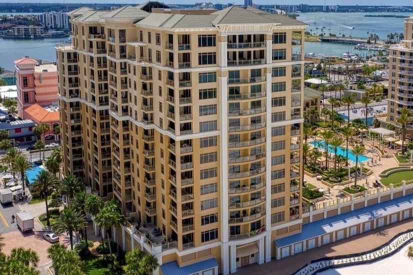 A multi-story residential building overlooks a swimming pool surrounded by palm trees and lounge chairs — 11 BAYMONT STREET UNIT 608, CLEARWATER BEACH, FL