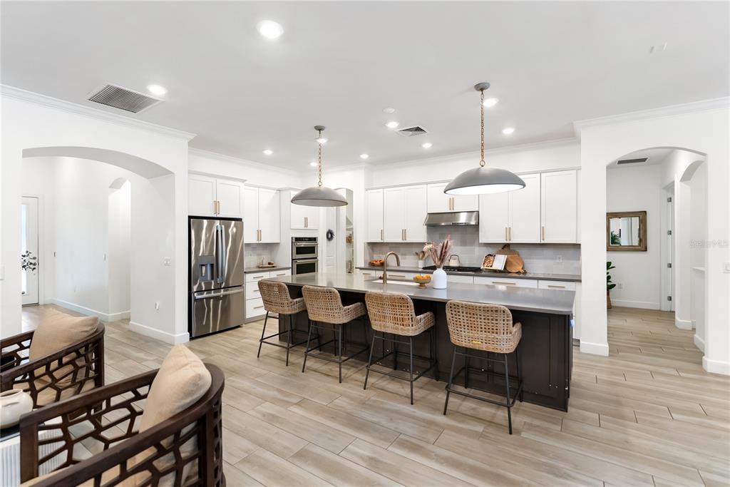 A modern kitchen features white cabinetry, a dark island with four wicker stools, and tile flooring — 12215 PORTSMOUTH TERRACE, BRADENTON, FL