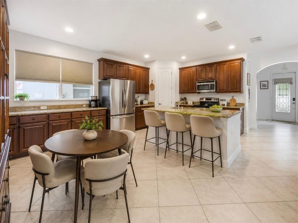 A kitchen with dark wood cabinets, granite countertops, a center island, and a dining table — 14542 BLACK CHERRY TRAIL, WINTER GARDEN, FL