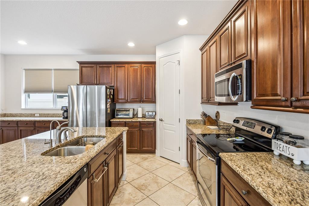 A kitchen features dark wood cabinets, granite countertops, stainless steel appliances, and tile flooring — 14542 BLACK CHERRY TRAIL, WINTER GARDEN, FL
