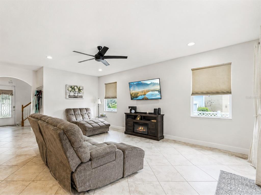 A living room features tile flooring, a ceiling fan, a fireplace console, and gray furniture — 14542 BLACK CHERRY TRAIL, WINTER GARDEN, FL