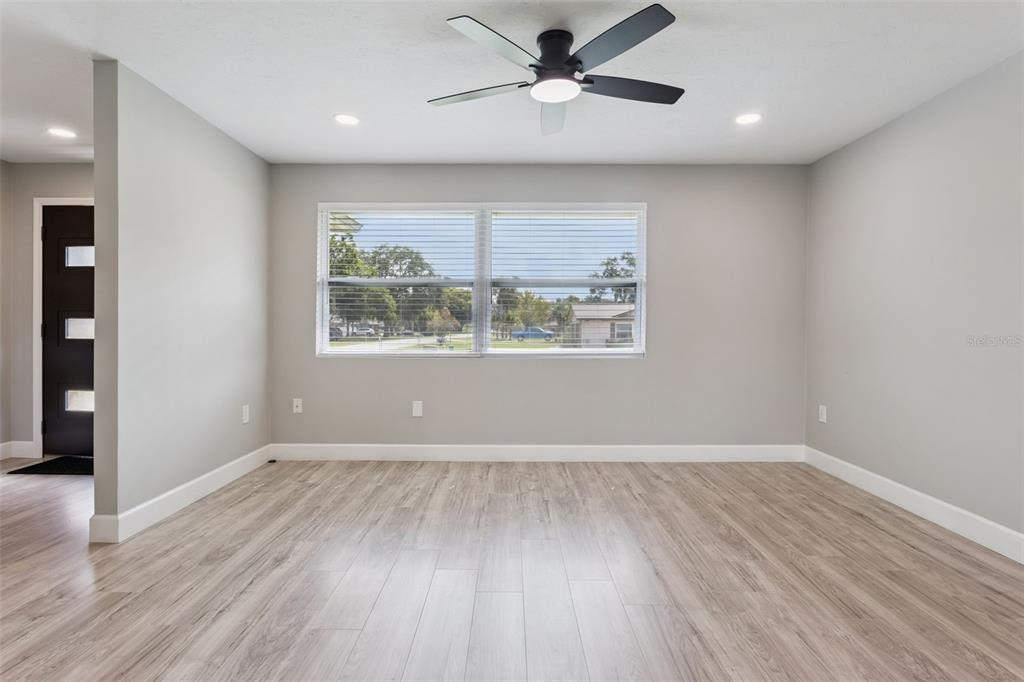 An empty room with light gray walls, wood-look flooring, a ceiling fan, and a large window — 33241 FAIRWAY ROAD, LEESBURG, FL