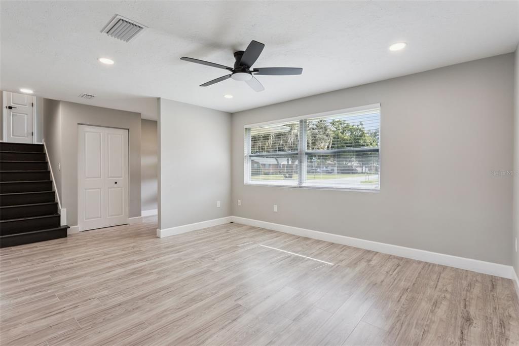 A bright room features light wood-look flooring, gray walls, a ceiling fan, and a staircase — 33241 FAIRWAY ROAD, LEESBURG, FL