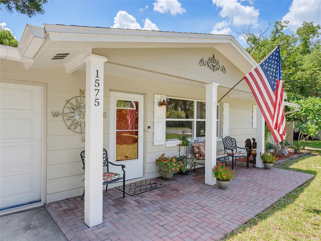 A single-story house exterior features a brick porch, an American flag, and a compass decoration — 1575 JASMINE WAY, CLEARWATER, FL