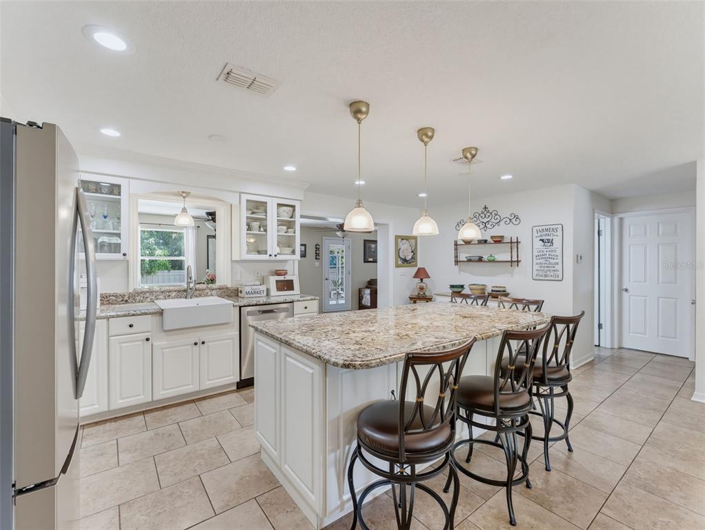 A kitchen features white cabinets, granite countertops, a farmhouse sink, and a central island — 1575 JASMINE WAY, CLEARWATER, FL