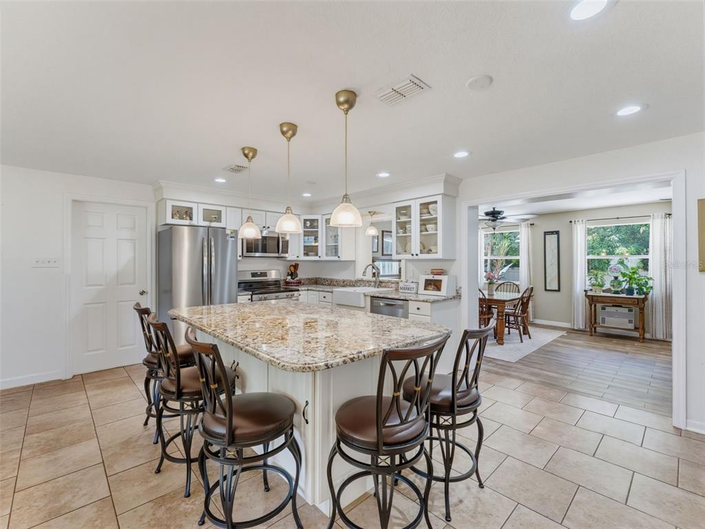 A kitchen features a granite-topped island with bar stools, white cabinetry, and tile flooring — 1575 JASMINE WAY, CLEARWATER, FL