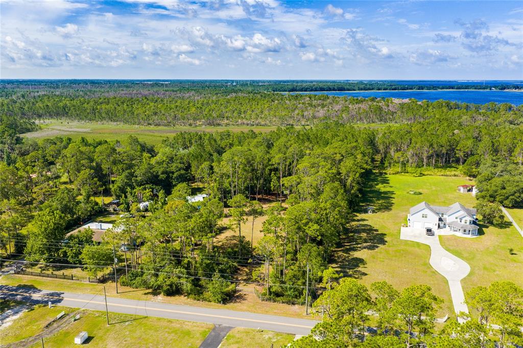 An aerial view shows a house, a wooded area, and a road near water — BASS HIGHWAY, ST CLOUD, FL
