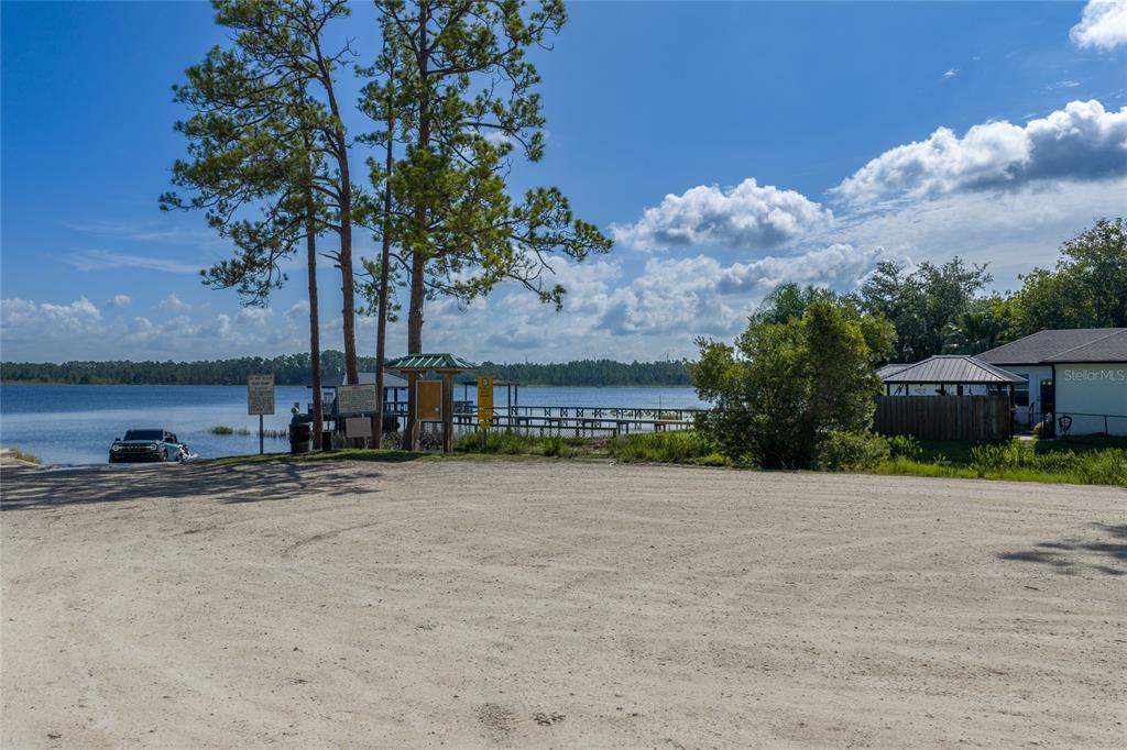 A sandy boat launch area sits beside a lake with a wooden dock and trees — BASS HIGHWAY, ST CLOUD, FL