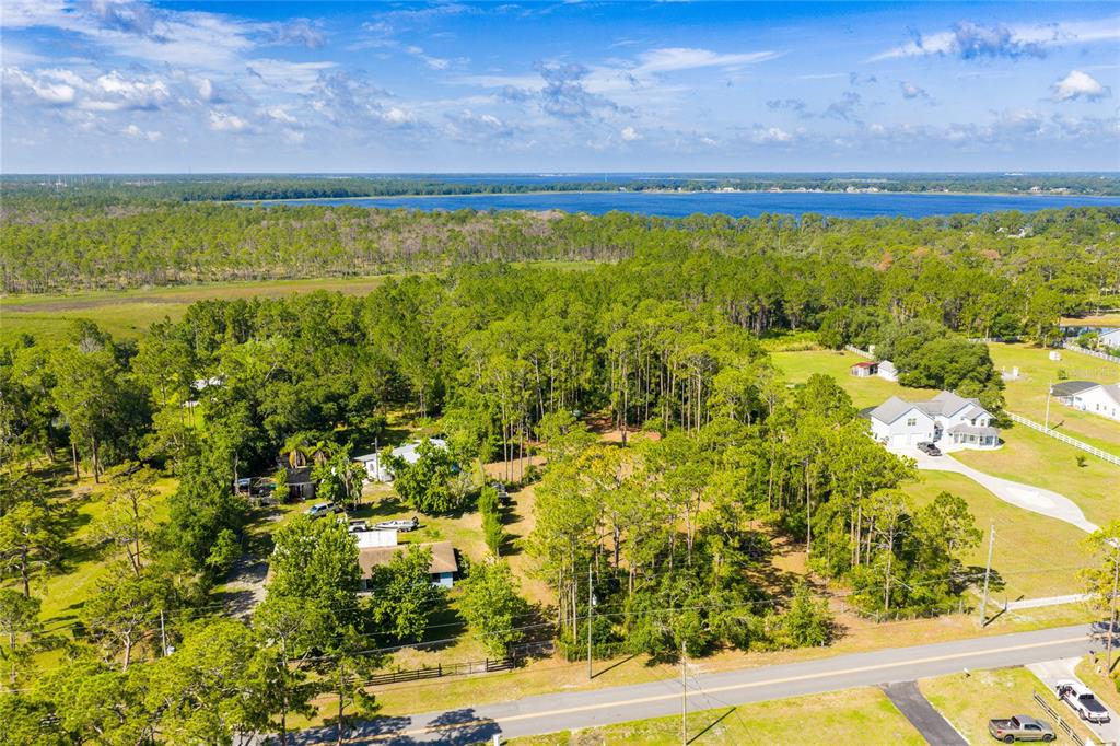 An aerial view shows a wooded residential lot with a house near a large lake — BASS HIGHWAY, ST CLOUD, FL