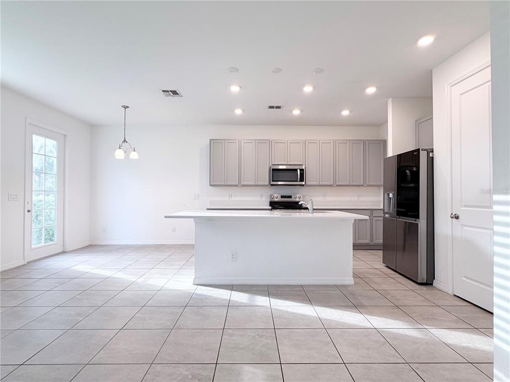 A kitchen features a white island, gray cabinets, stainless steel appliances, and light tile flooring — 1542 DISCOVERY STREET, DAVENPORT, FL