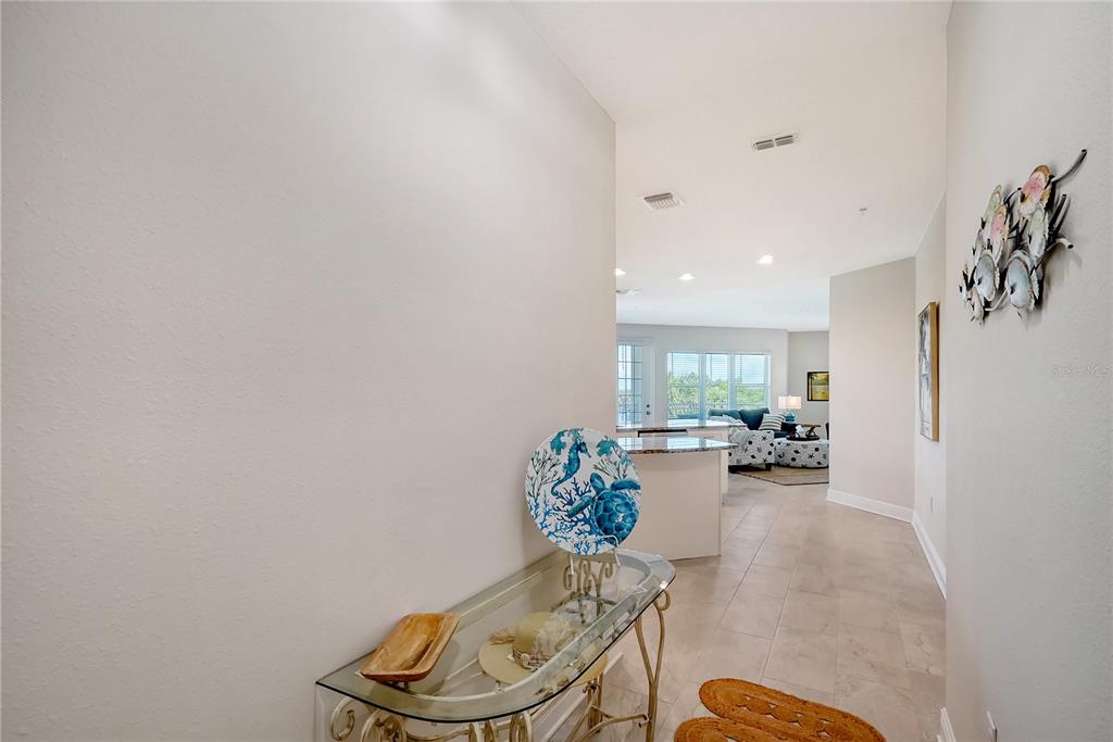A hallway with a glass console table leads into an open-concept kitchen and living area — 7930 34TH AVENUE W UNIT 102, BRADENTON, FL