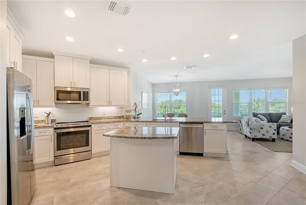 A kitchen with white cabinets, stainless steel appliances, and a granite-topped island opens to a living area — 7930 34TH AVENUE W UNIT 102, BRADENTON, FL
