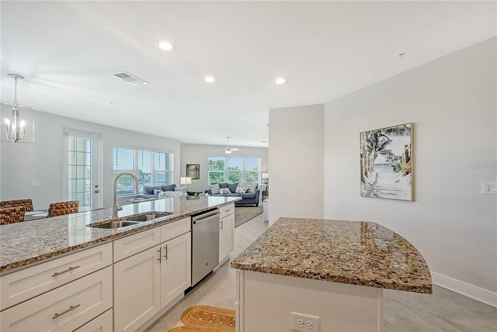 A kitchen with granite countertops and white cabinets opens into a living room area — 7930 34TH AVENUE W UNIT 102, BRADENTON, FL