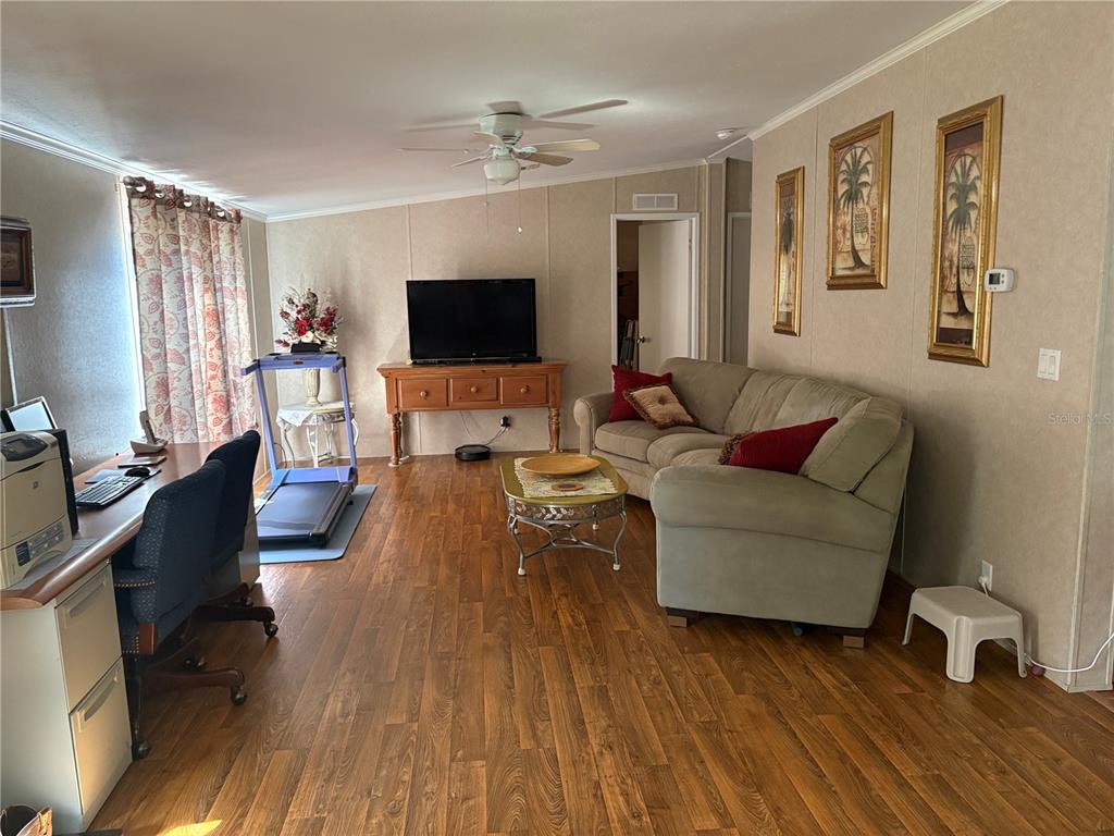 A living room features wood-look flooring, a beige sofa, a treadmill, and a desk area — 10342 SHADY DRIVE, HUDSON, FL