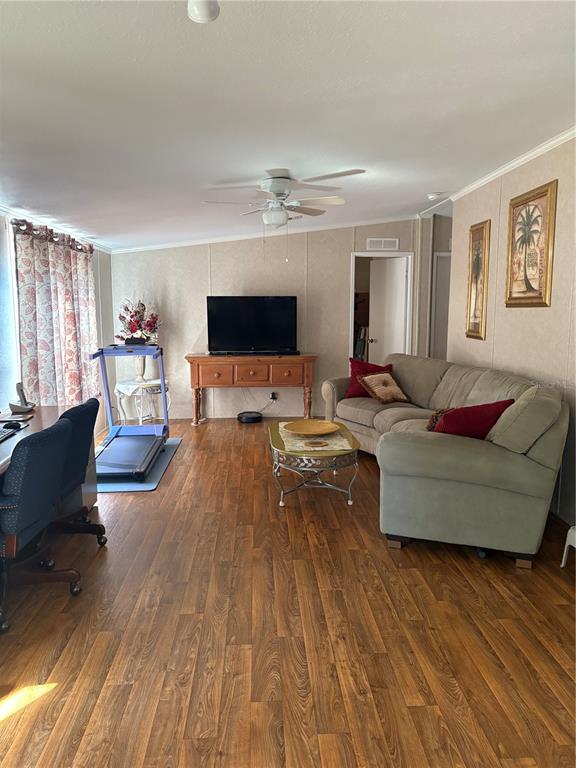 A living room features wood-look flooring, a beige sofa, a television on a wooden console, and a treadmill — 10342 SHADY DRIVE, HUDSON, FL