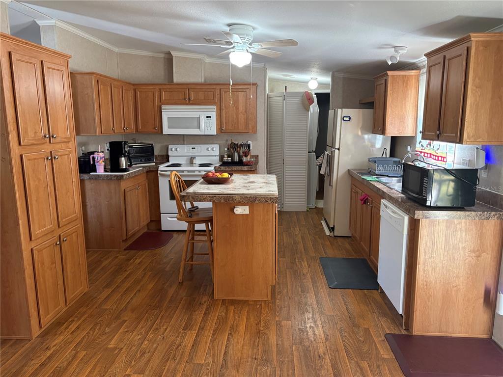 A kitchen features wood cabinets, a central island with seating, and white appliances — 10342 SHADY DRIVE, HUDSON, FL