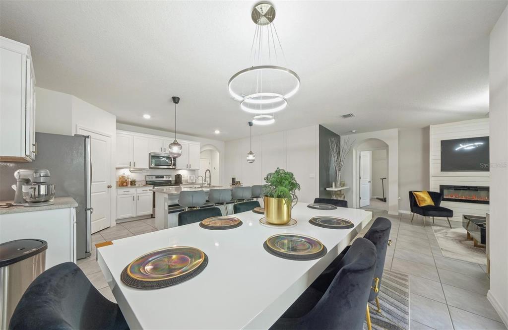 A modern open-concept kitchen and dining area features white cabinetry, a large island, and chandelier — 160 HICKORY COURSE LOOP, OCALA, FL