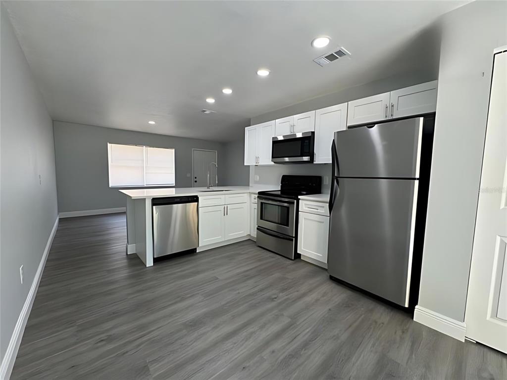 A modern kitchen features white cabinets, stainless steel appliances, and gray wood-look flooring — 442 S HILL AVENUE, DELAND, FL
