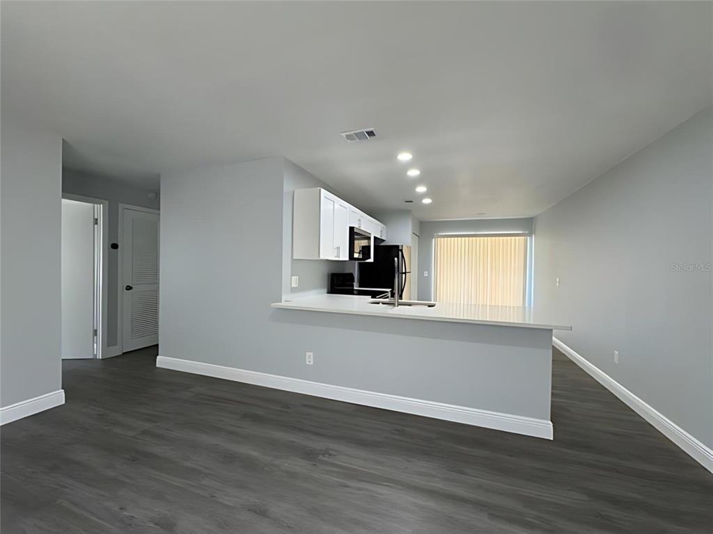 A kitchen with white cabinets and a breakfast bar overlooks a room with gray flooring — 442 S HILL AVENUE, DELAND, FL