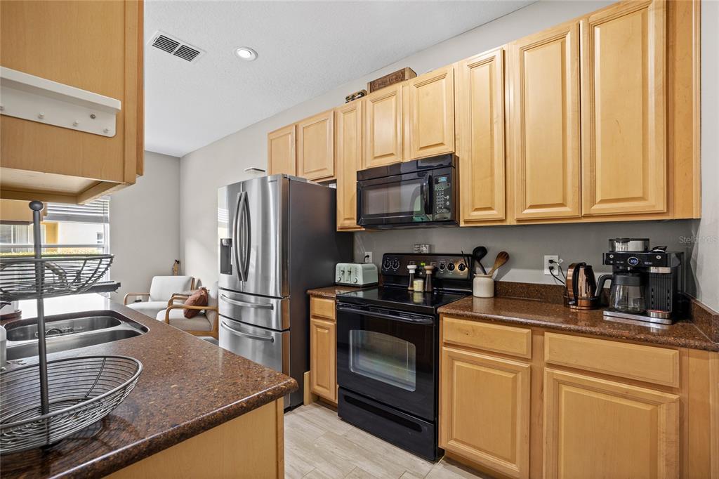 A kitchen features light wood cabinets, dark granite countertops, stainless steel appliances, and tile flooring — 723 MAROTTA LOOP, OCOEE, FL