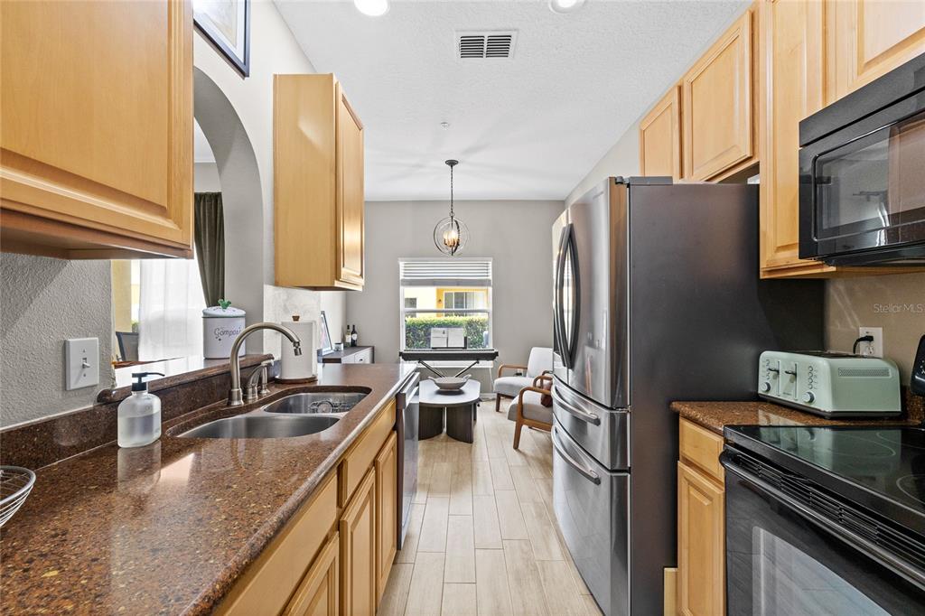 A kitchen with wood cabinets, granite countertops, and stainless steel appliances leads to a dining area — 723 MAROTTA LOOP, OCOEE, FL