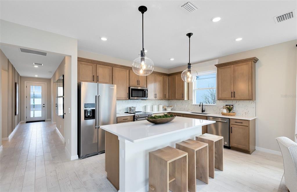 A kitchen features light wood cabinets, a white quartz island with stools, and stainless steel appliances — 2639 CLEAR NIGHT AVENUE, KISSIMMEE, FL