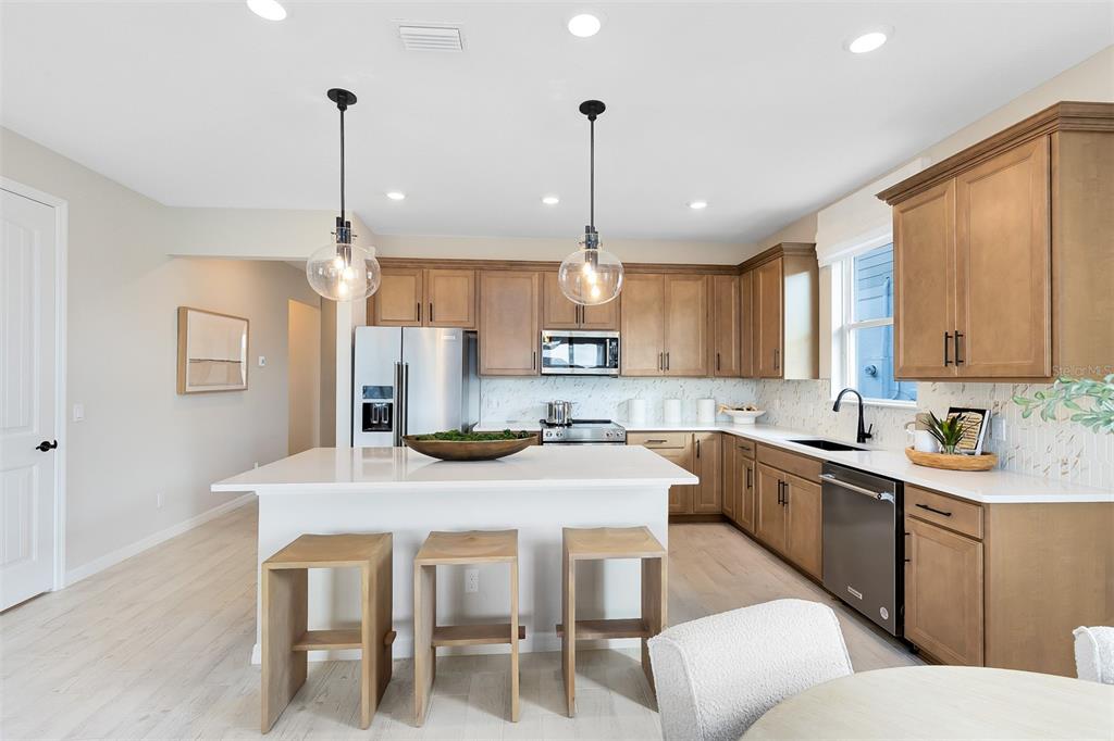 A kitchen features light wood cabinets, a white island with three stools, and stainless appliances — 2639 CLEAR NIGHT AVENUE, KISSIMMEE, FL