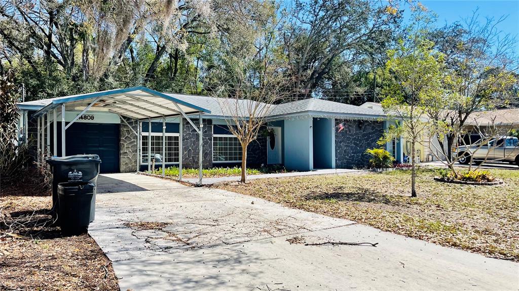 A single-story house with a stone facade, a metal carport, and a concrete driveway — 14809 TULIP DRIVE, TAMPA, FL