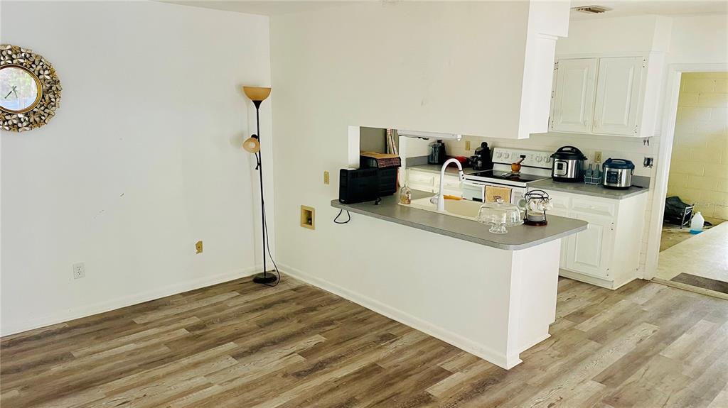 A kitchen with white cabinets and a breakfast bar overlooks a room with wood-look flooring — 14809 TULIP DRIVE, TAMPA, FL