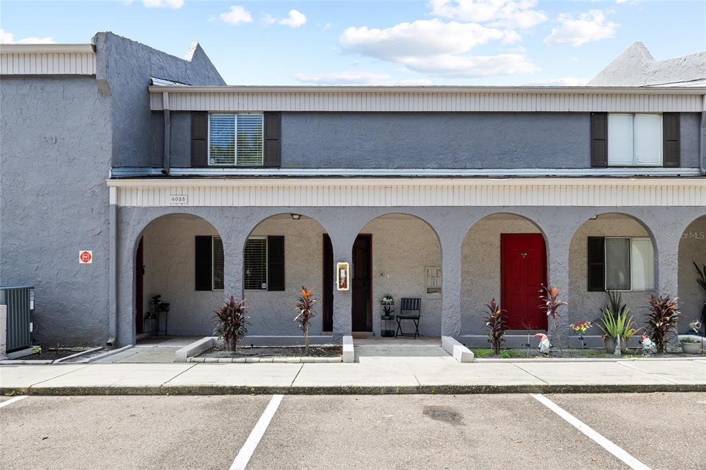 A gray two-story townhouse exterior features a covered arched walkway and a red front door — 4038 CORTEZ DRIVE UNIT B, TAMPA, FL