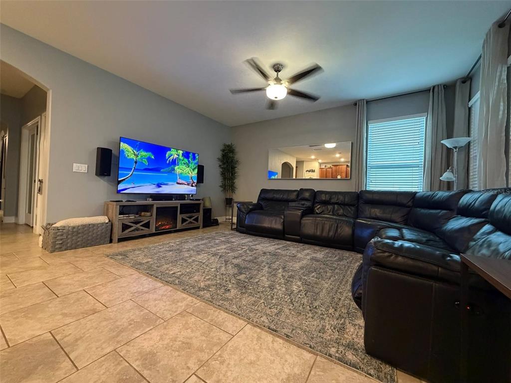 A living room features a large sectional sofa, a wall-mounted television, and tile flooring — 4419 LINWOOD TRACE LANE, CLERMONT, FL