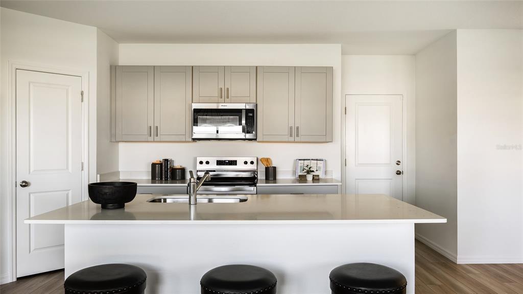 A modern kitchen features a central island with bar seating, light gray cabinets, and stainless-steel appliances — 33824 NOBLE CREEK PLACE, DADE CITY, FL