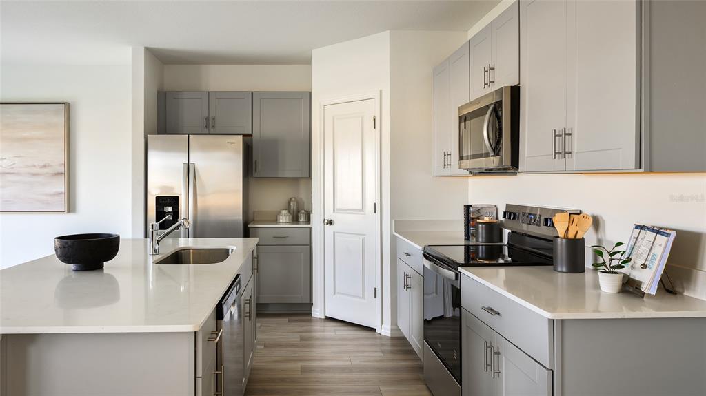 A modern kitchen features gray cabinets, white quartz countertops, stainless steel appliances, and a central island — 33824 NOBLE CREEK PLACE, DADE CITY, FL