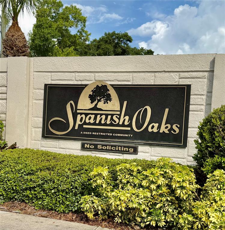A sign for a deed-restricted community named Spanish Oaks is mounted on a stone wall — 1011 WINDING OAKS DRIVE, PALM HARBOR, FL