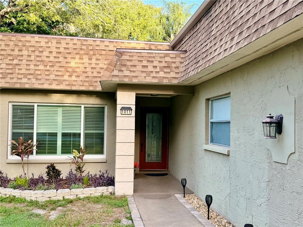 The exterior of a house features a red front door, a large window, and landscaping — 1011 WINDING OAKS DRIVE, PALM HARBOR, FL