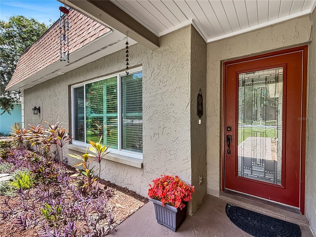 A tan stucco house exterior features a red front door and a large window — 1011 WINDING OAKS DRIVE, PALM HARBOR, FL