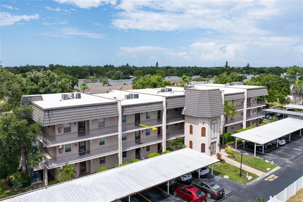 An aerial view of a multi-story apartment building with covered parking and a yellow arrow — 209 CORDOVA GREEN UNIT 209, SEMINOLE, FL