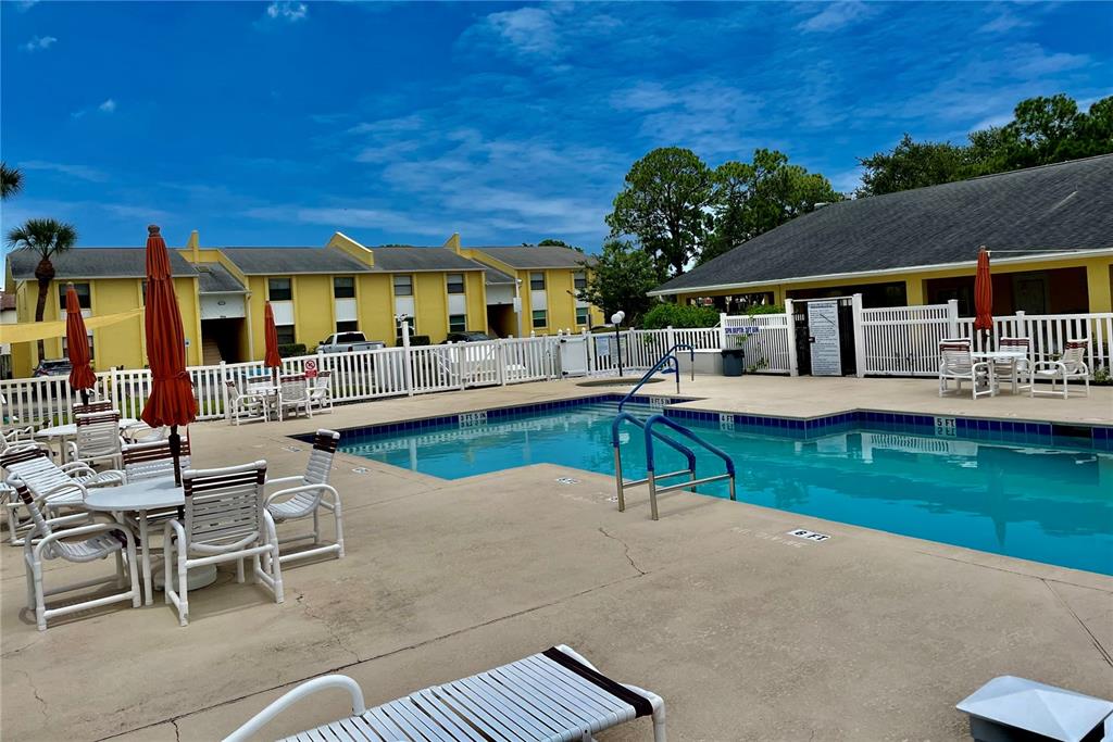 A swimming pool with lounge chairs and umbrellas sits in front of yellow apartment buildings — 594 N WICKHAM ROAD UNIT 2, MELBOURNE, FL