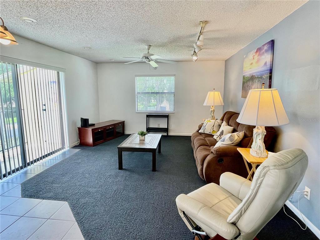 A living room features dark carpeting, a brown sofa, a white recliner, and sliding glass doors — 594 N WICKHAM ROAD UNIT 2, MELBOURNE, FL