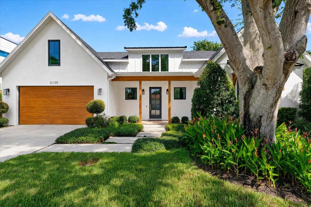 A white house with a wood garage door, a front porch, and a large tree — 2135 DATURA STREET, SARASOTA, FL