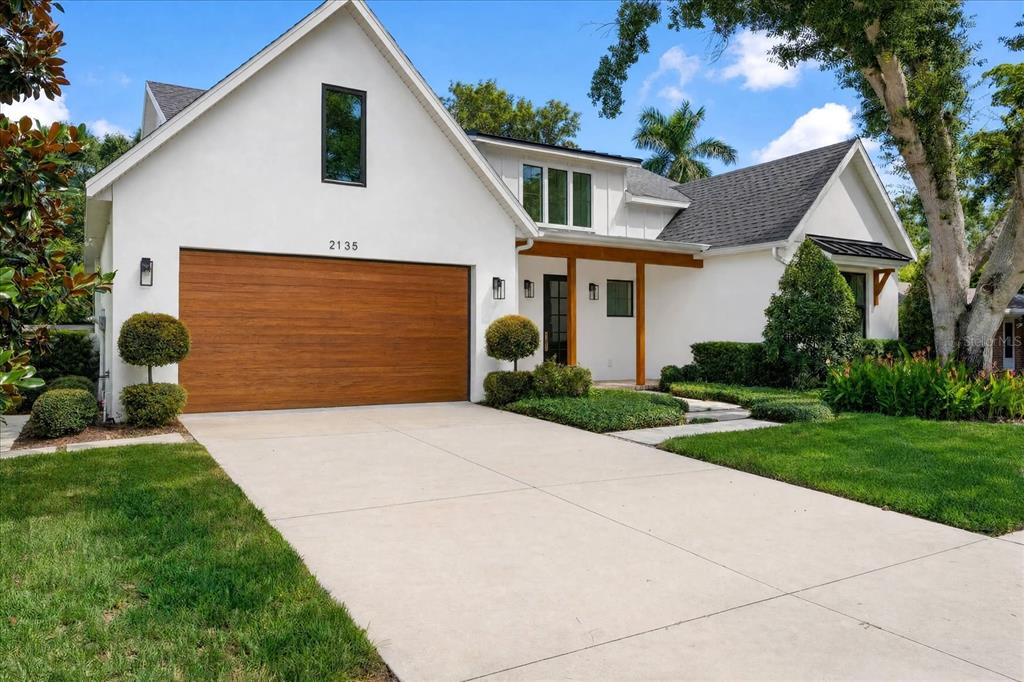 A white house with a wood-paneled garage door and a covered front entryway — 2135 DATURA STREET, SARASOTA, FL