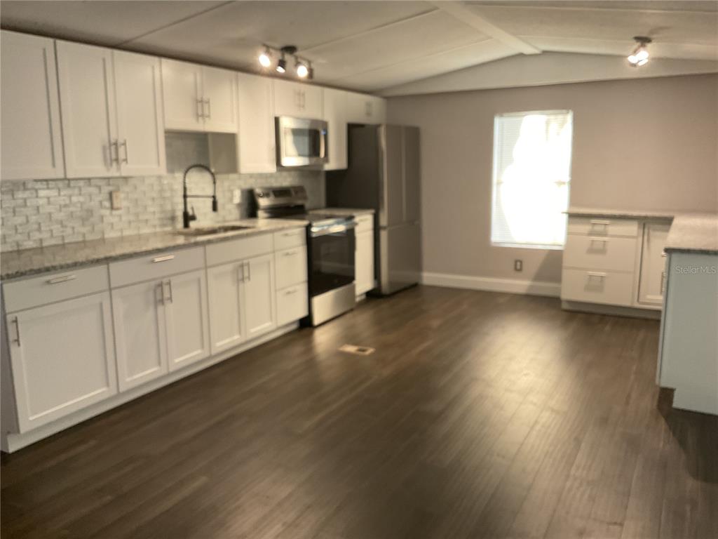 A kitchen features white cabinets, stainless steel appliances, a tile backsplash, and dark wood flooring — 5038 NE SANDY ROAD, ARCADIA, FL