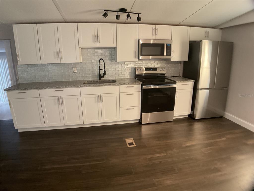 A kitchen features white cabinets, stainless steel appliances, a gray backsplash, and dark wood flooring — 5038 NE SANDY ROAD, ARCADIA, FL