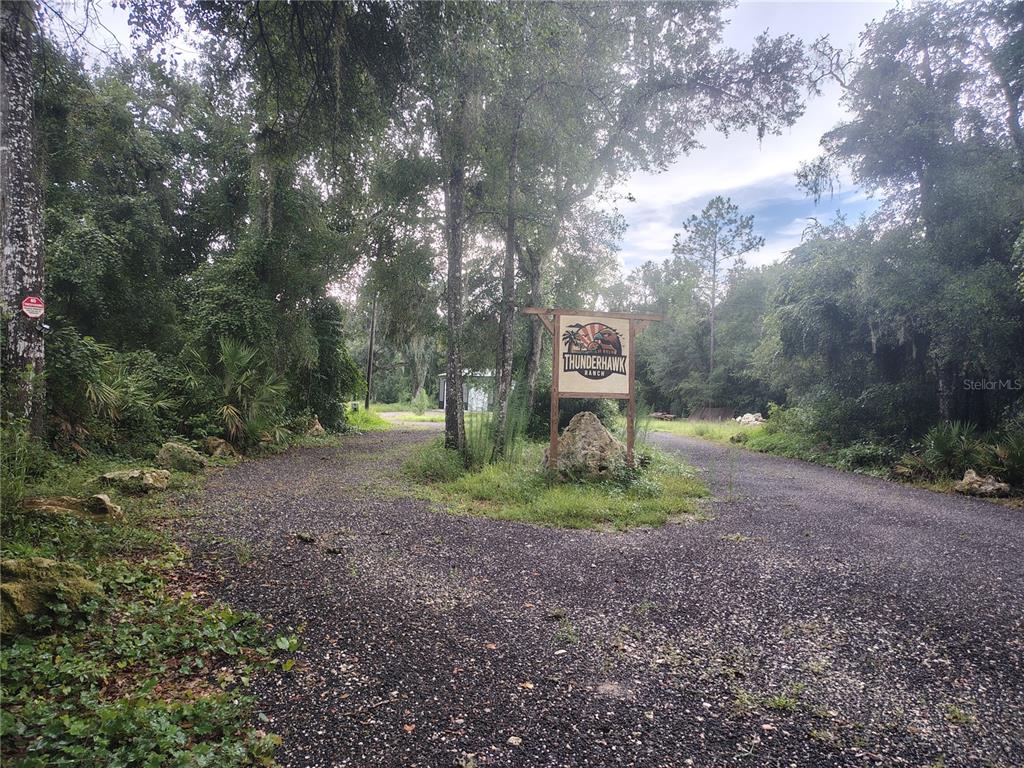 A gravel driveway forks around a Thunderhawk Ranch sign in a wooded area — 12537 SW 38TH WAY, WEBSTER, FL