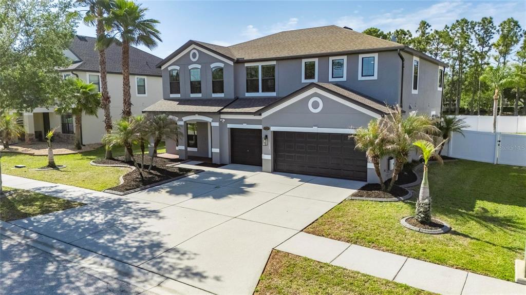 A two-story gray house with a three-car garage and palm trees in the front yard — 11807 HARPSWELL DRIVE, RIVERVIEW, FL