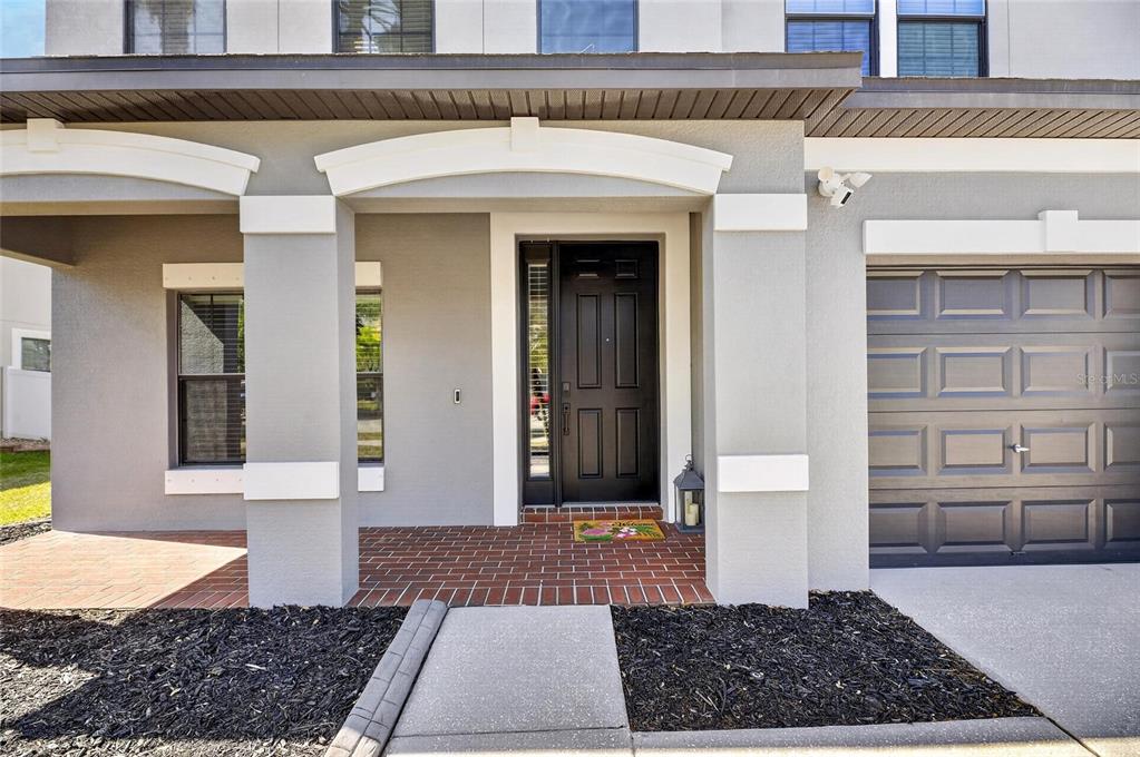 The exterior of a house features a dark front door, brick porch, and gray siding — 11807 HARPSWELL DRIVE, RIVERVIEW, FL