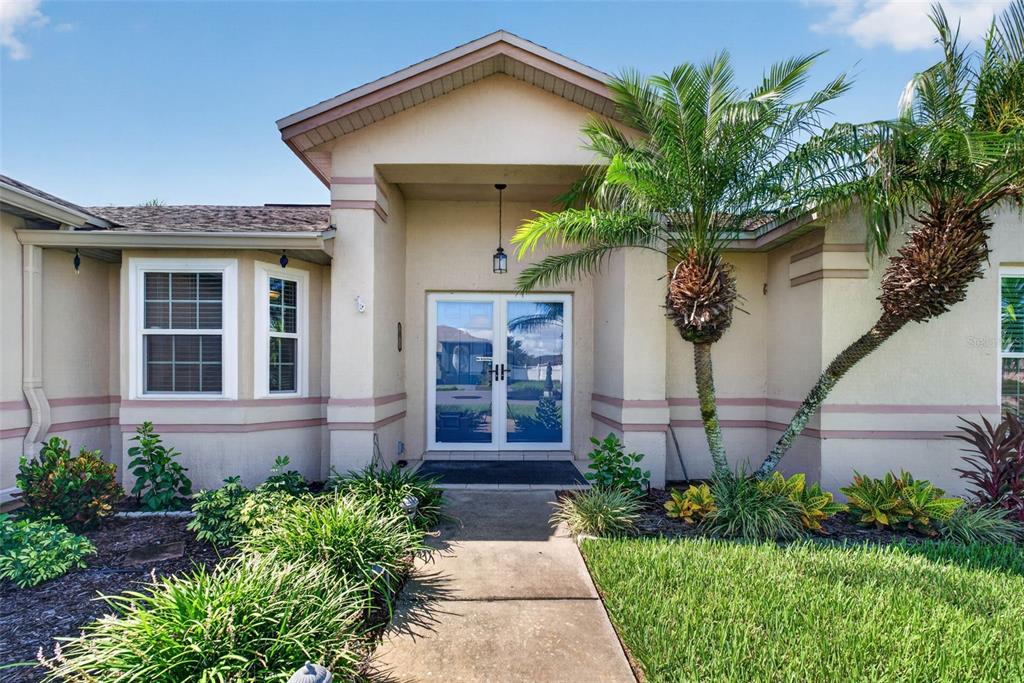 A concrete walkway leads to the double front doors of a tan stucco house — 706 HIGHLAND CREST LOOP, LAKE WALES, FL